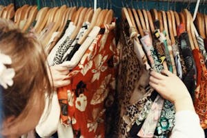 a person looking through hung clothes at a thrift store