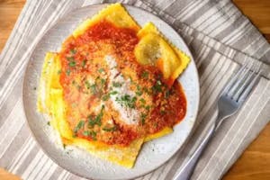 A plate with ravioli and red sauce topped with parmesan and fresh parsley