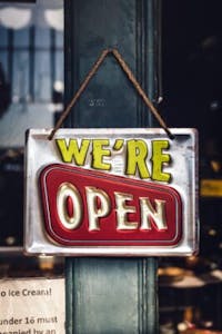 a metal sign that is silver, yellow and red, that says "We're Open" hanging on a door.
