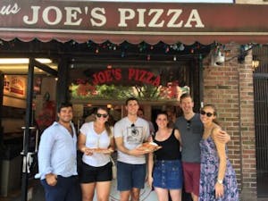 Friends standing at Joe's Pizza entrance with large slices of New York style pizza