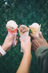 three hands holding out different flavors of ice cream cones