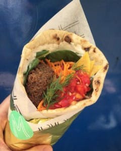 a close up of a pita with falafel, fresh dill, and veggies