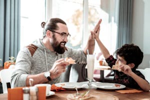 A father and son high fiving while eating at a restaurant 