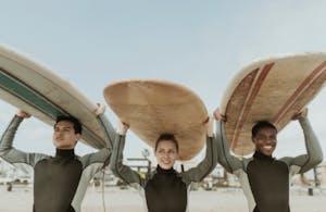 Three people holding surfboards on their heads