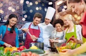 A group of people wearing colorful aprons standing with a chef taking a cooking class