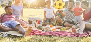 Young parents having fun with their children in summer time eating, laughing and playing together at the park