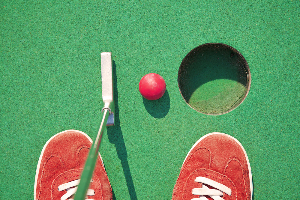 An over view of a golf cup, red ball and and a small put next to red shoes