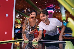 Two adults playing air hockey at an arcade smiling