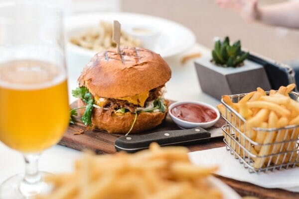 a plate of food on a table, a burger, two orders of fries, and a beer