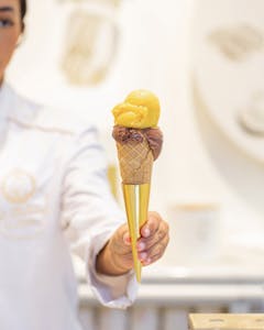 a hand holding an ice cream cone with a gold tip 