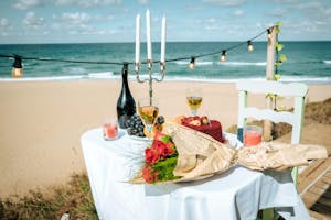 food and wine and roses on a table on the coast with beach in background