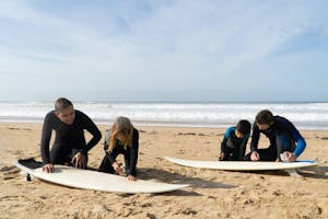 a group of people sitting at a beach waxing their surfboards