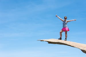 Brave young adult woman hiker stands on top of Potato Chip Rock in San Diego California