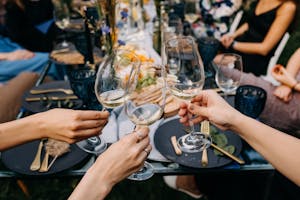 Women raising glasses with white wine at an open air party with friends and family.