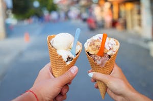 hands holding ice cream cones with bright colored spoons