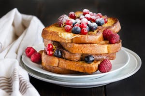 Traditional French toast with berries: blueberries, currant, raspberries and icing sugar for perfect sweet breakfast. Delicious dessert background.