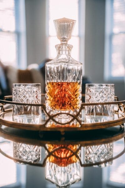 a glass decanter of whiskey sitting on a tray with two glasses on a table