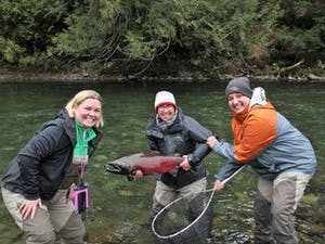 A group of people hold a fish they caught fly fishing.