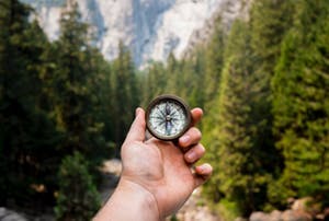 Hand holding a compass, mountains in background