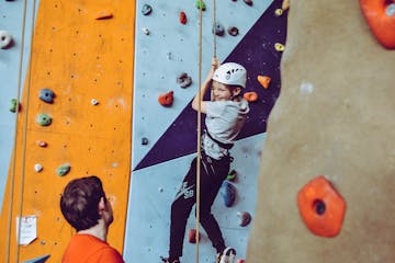 A child practices rappelling from a climbing wall with an instructor nearby
