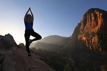 A woman practicing yoga atop the Canyon Overlook Trail during the Zion Sunrise Hike