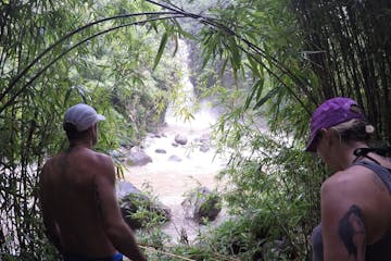 A couple hiking in Hana, surrounded by green vegetation and approaching a waterfall