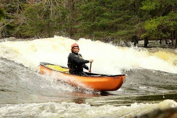 a paddler surfing a standing wave on the Madawaska River in an orange solo canoe