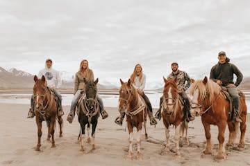 a group of people riding horses on a beach