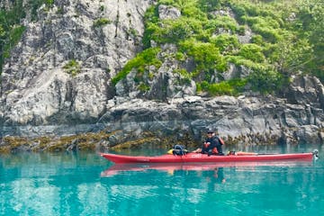 A kayak guide in a single kayak glides through turquoise waters near the coastline