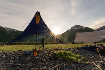 Two kitchen tarps set up with kayak paddles supporting them on a rocky beach with driftwood