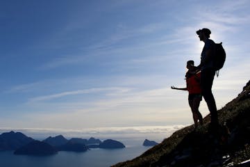 Two people stand on a mountain with a view of the barrier islands and Gulf of Alaska