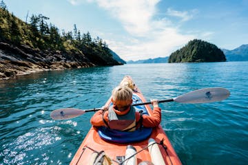 A child sits in the front seat of a double sea kayak in Resurrection Bay on a private family kayak tour