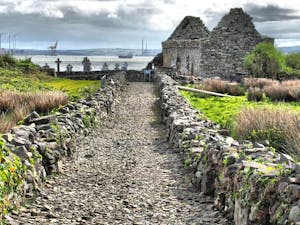 Image of the well path leading down to Teampeall na Marbh on Scattery Island with the towers of Moneypoint power station in the background.