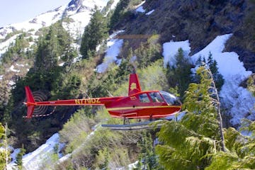 A red helicopter flying near a mountain.