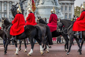 Six guards in red capes on black horses in front of Buckingham Palace