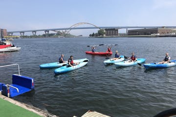 A group of kayakers launching in single kayaks on Lake Michigan. The bridge is in the background.