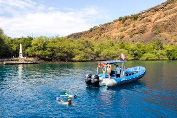 aerial view of a boat sitting in the ocean near the captain cook monument with snorkelers in the water nearby