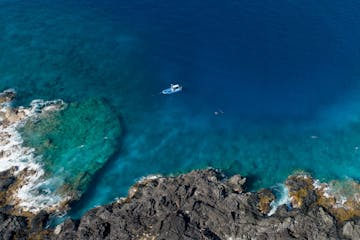 aerial of boat near rugged lava coast in hawaii with pristine waters