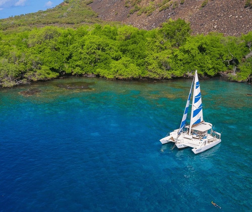 a catamaran sits in the beautiful calm water off of the rugged big island coastline in Kealakekua bay Hawaii