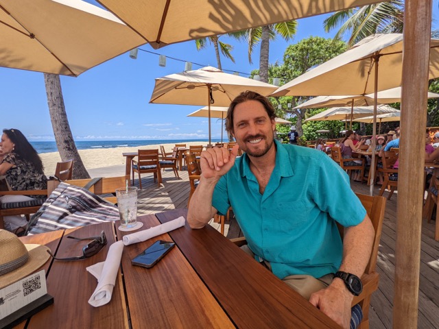 Byron Kay sitting at a table with a blue umbrella