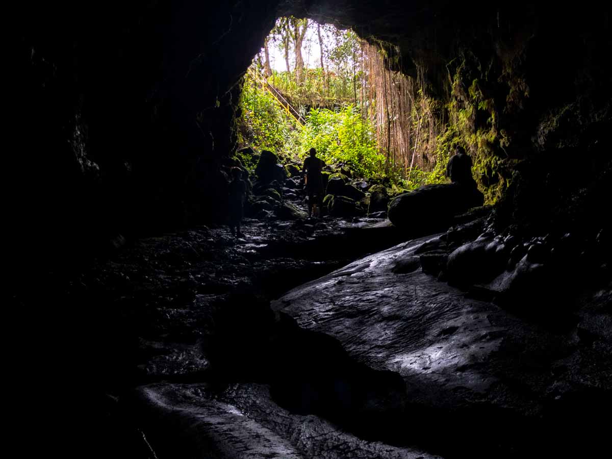 inside a lava tube cave looking out towards the entrance with a few people standing near the entrance