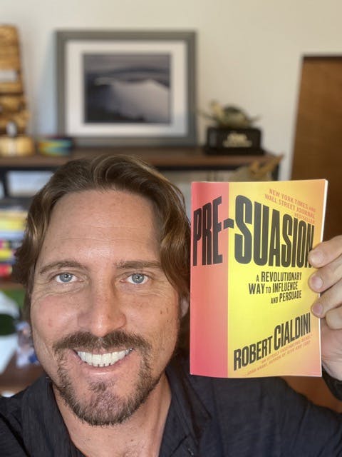 headshot of Byron Kay smiling for the camera holding the book pre-suasion