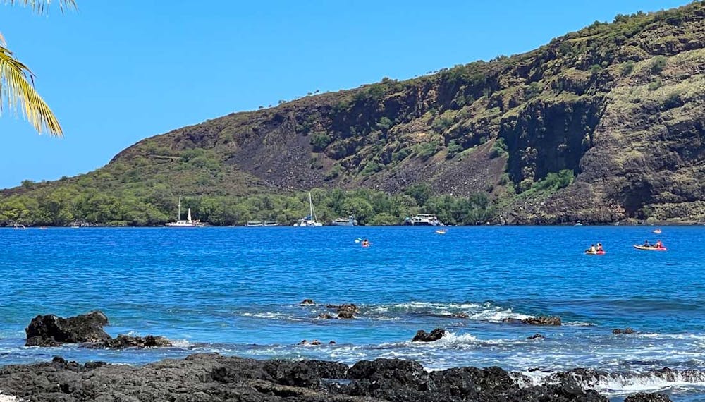 view of the captain cook monument on the far side of kealakekua bay looking from manini beach on the opposite side. Kayaks and boats are in between in the sea