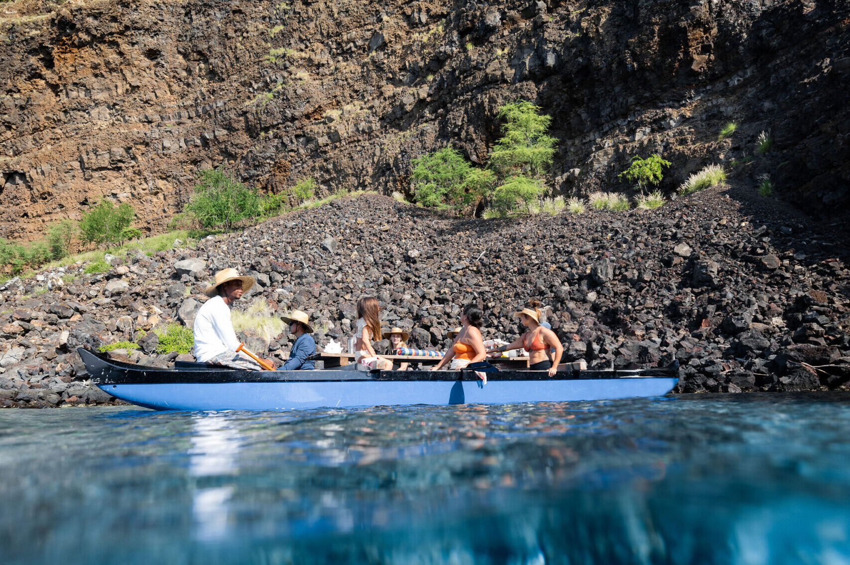 people sitting in a double hulled canoe in the ocean in front of a steep cliff