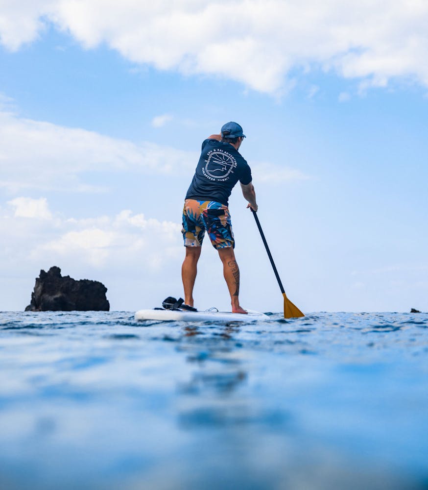 a man stands on a paddleboard on the ocean while paddling with a rock behind
