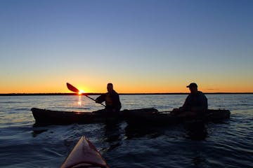 A group of people paddling kayaks during a sunset on a lake