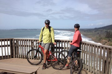 Two bikers leaning against lookout platform overlooking the sea