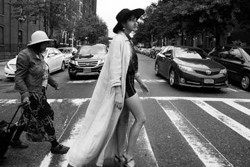 black and white photo of woman walking across a crosswalk wearing trendy clothing