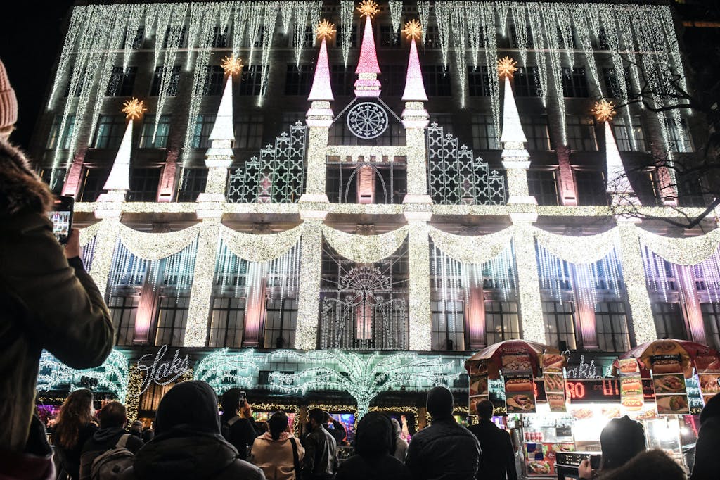 Saks fifth avenue flagship building covered in holiday lights with people watching it