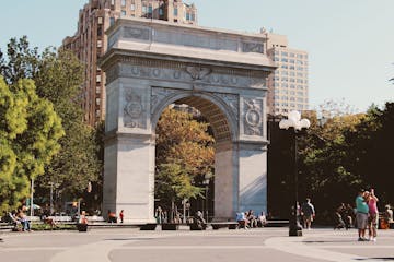 a group of people walking in front of a statue with Washington Square Park in the background